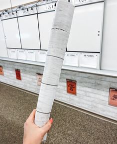 a person holding up a large piece of paper in front of a wall with calendars on it