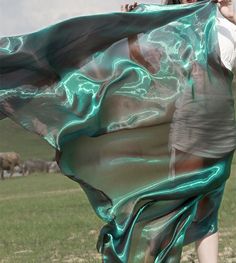 a woman is walking in the grass with a scarf around her