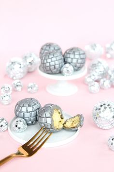 a fork is laying on a plate next to some silver balls and one has a bite taken out of it