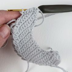 someone is crocheting the end of a knitted sock with a golden needle