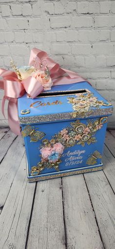 a blue box with pink bows on it sitting on a wooden floor next to a brick wall