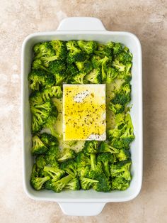 broccoli and other vegetables in a white dish with a square piece of cheese on top