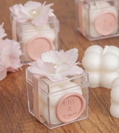 small candles with flowers in them on a wooden table next to some waxed soaps