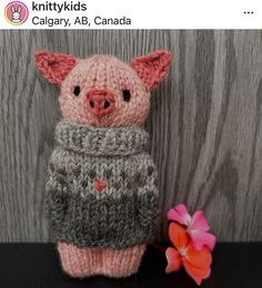 a small knitted pig sitting next to a pink flower