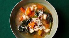 a white bowl filled with soup and vegetables on top of a green tableclothed surface