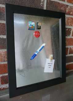 a pen and some stickers are on a glass frame with a brick wall in the background