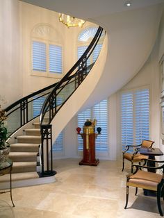 an elegant staircase in a house with white walls and windows, along with a clock on the table