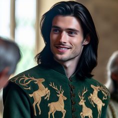 a man with long black hair wearing a green jacket and gold deer designs on it