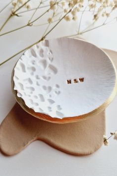 a white plate with two small gold letters on it and some flowers in the background