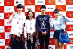 four people standing in front of a red and white wall giving the peace sign with their fingers