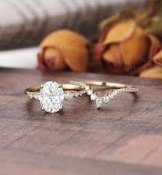 two gold rings with diamonds on them sitting on a wooden table next to rose petals