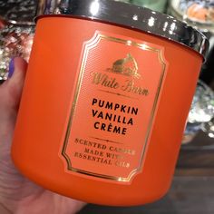 a hand holding an orange candle that says pumpkin vanilla creme