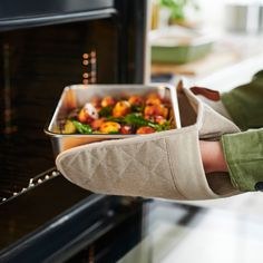 a person is holding a pan with food in it while standing next to an oven