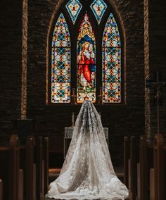 the bride's veil is covering her face in front of an ornate stained glass window