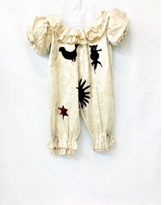 a baby's white romper with black cats and stars on it, hanging from a wall