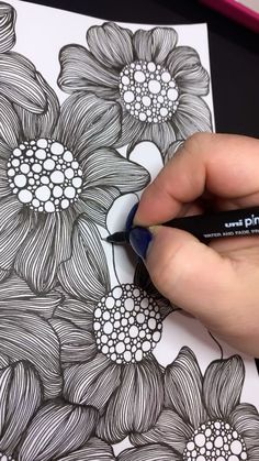 a person is drawing flowers on a piece of paper with a marker and some pens