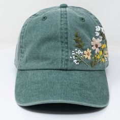 a green hat with flowers embroidered on the front and back side, sitting on a white surface