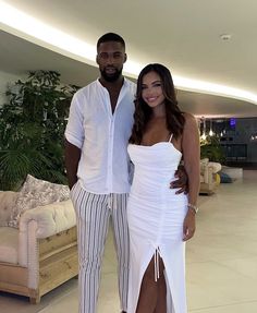 a man and woman standing next to each other in front of a living room filled with furniture