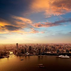 an aerial view of a large city and the ocean with boats on it at sunset