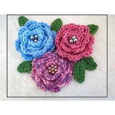 three crocheted flowers with green leaves on white background, one is blue and the other is pink