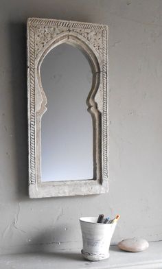 a white vase sitting on top of a table next to a mirror and a cup