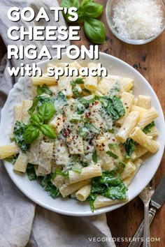 a white plate topped with pasta and spinach next to a bowl of parmesan cheese