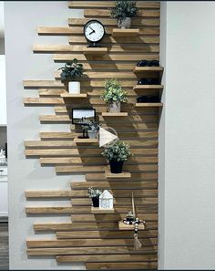 a wooden shelf with plants and clocks on it in a room that has white walls