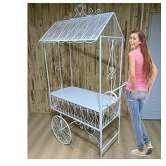 a woman standing next to a white metal doll cart with a canopy on it's side