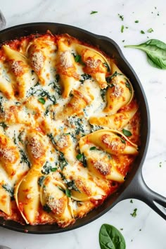 a skillet filled with ravioli and spinach covered in parmesan cheese