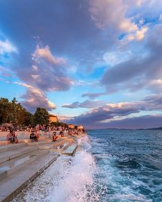 people are sitting on the steps near the water as the sun sets over the ocean