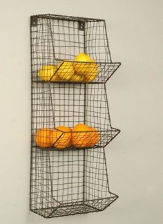 three wire baskets holding oranges and lemons are hanging on the wall in front of a white wall