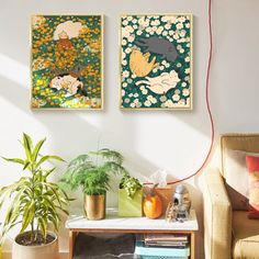 two paintings hang on the wall above a table with books and plants in front of it