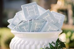 a white bowl filled with blue napkins on top of a table next to greenery