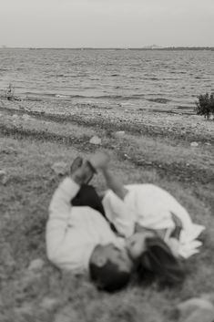 a man laying on the ground next to water with his head in his hands and another person standing behind him