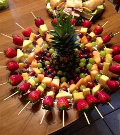 a pineapple surrounded by strawberries, grapes, and other fruit on skewers