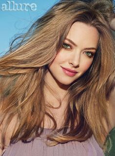 a woman with long brown hair and green eyes posing in front of a blue sky