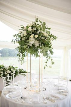 a table with white flowers and greenery on it is set for a formal function