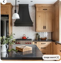 a kitchen with wooden cabinets and black counter tops, an island in the middle has a cutting board on it