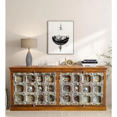 a wooden sideboard with glass doors and drawers in front of a painting on the wall