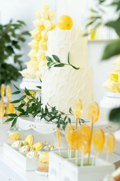 a white cake sitting on top of a table covered in lemons and cupcakes