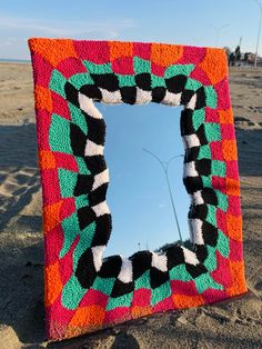 a square shaped mirror sitting on top of a sandy beach