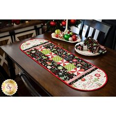 a christmas table runner on top of a wooden dining room table with plates and ornaments