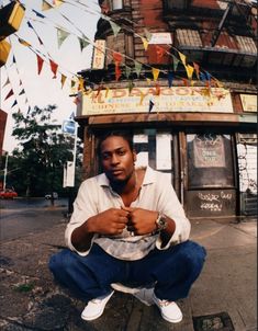 a man squatting on the ground in front of a building with flags hanging from it