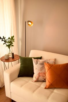 a living room with a white couch and some pillows on the sofa, next to a lamp