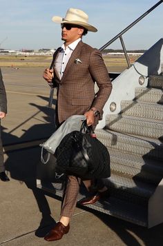 a man in a suit and hat is walking towards an airplane with his handbag