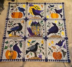 a quilted table topper with birds and pumpkins on it, sitting on the floor