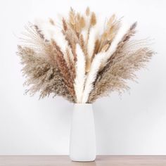 some dry grass in a white vase on a table