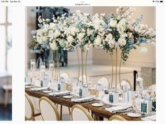 the table is set with white and blue flowers in tall vases on each side