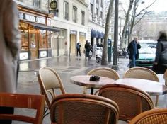 tables and chairs are set up outside on the sidewalk in front of buildings with people walking by