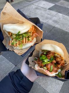 two sandwiches with meat and veggies in paper wrappers on the street side